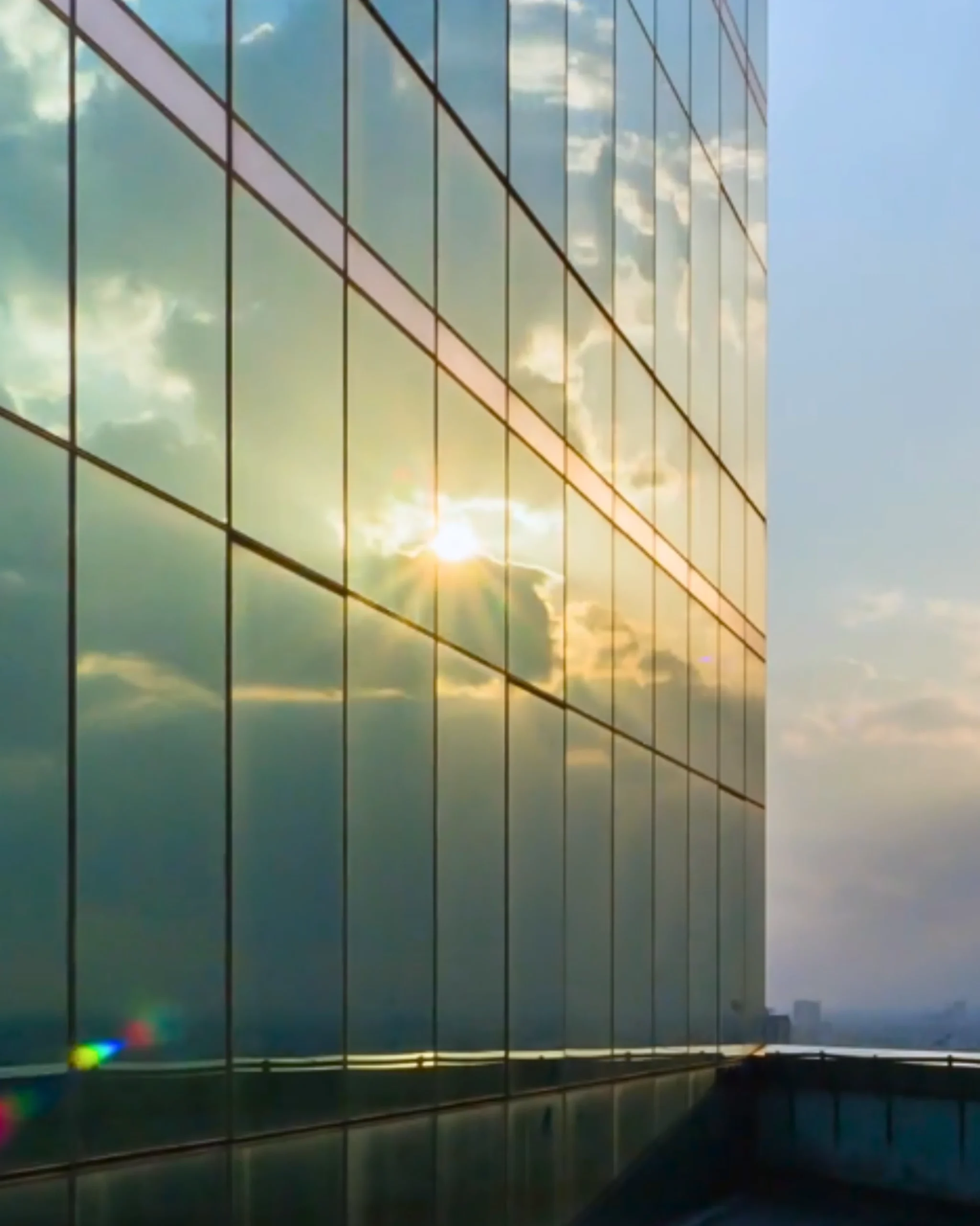 Façade d'un bâtiment vitré montrant le reflet du ciel et du soleil