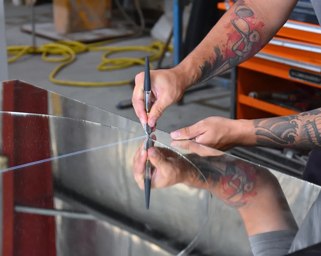 Dans l'atelier, le coupeur de verre utilise le diamant sur un miroir afin de le couper à la forme voulue, sa main et son outil se reflètent dans le miroir