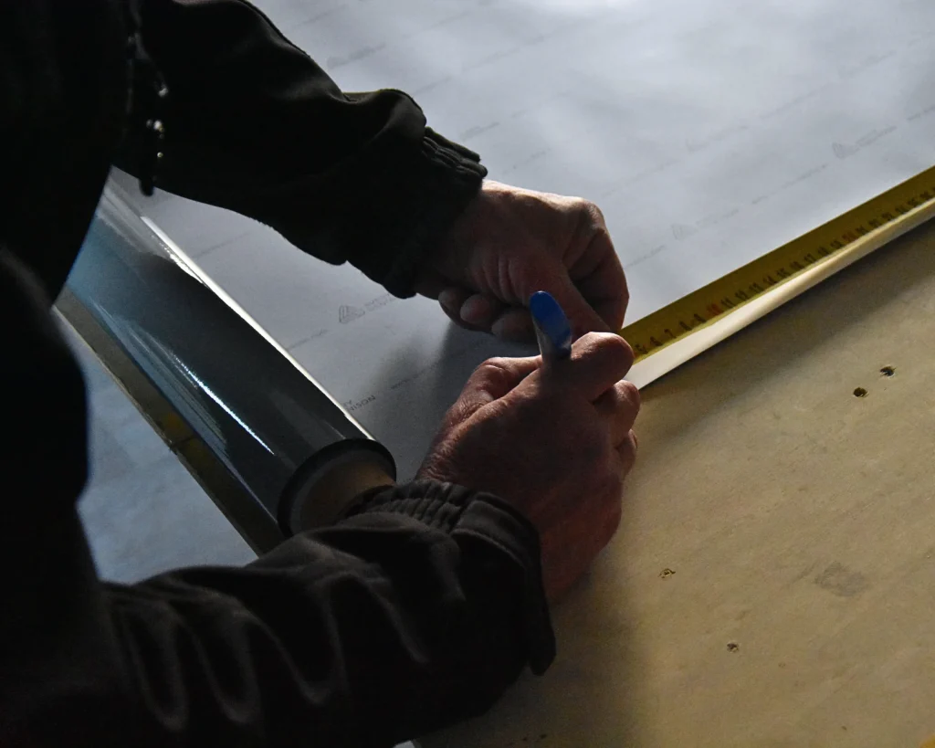 Technicien sur chantier mesurant un film à poser sur une fenêtre avant la découpe