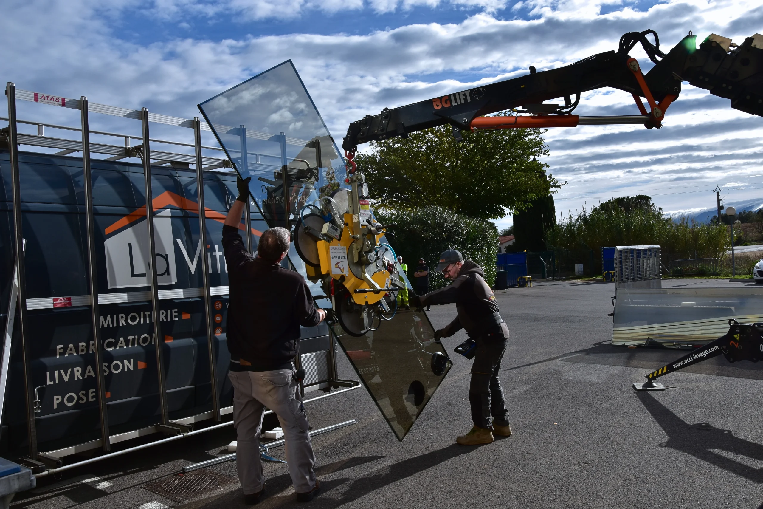 Deux techniciens aidés de la grue sont en train de poser l'ancien verre sur le fourgon de La Vitrerie lors du chantier à l'agglo sur le site de Canohès