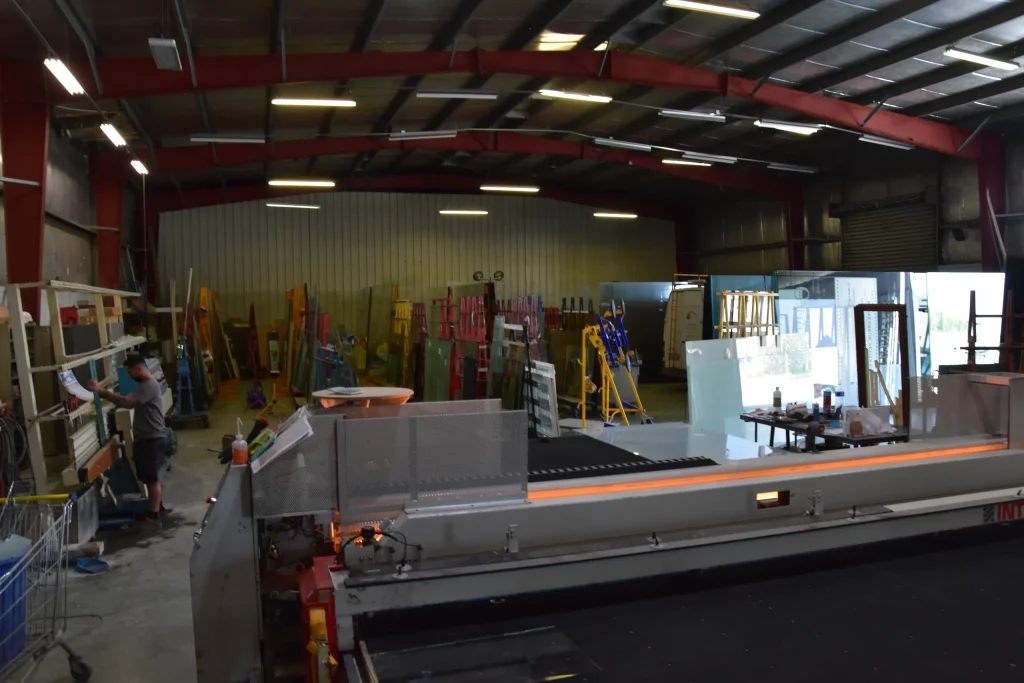 Vue d'ensemble de l'atelier de La Vitrerie, machine de découpe au premier plan et technicien sur la rectiligne à gauche